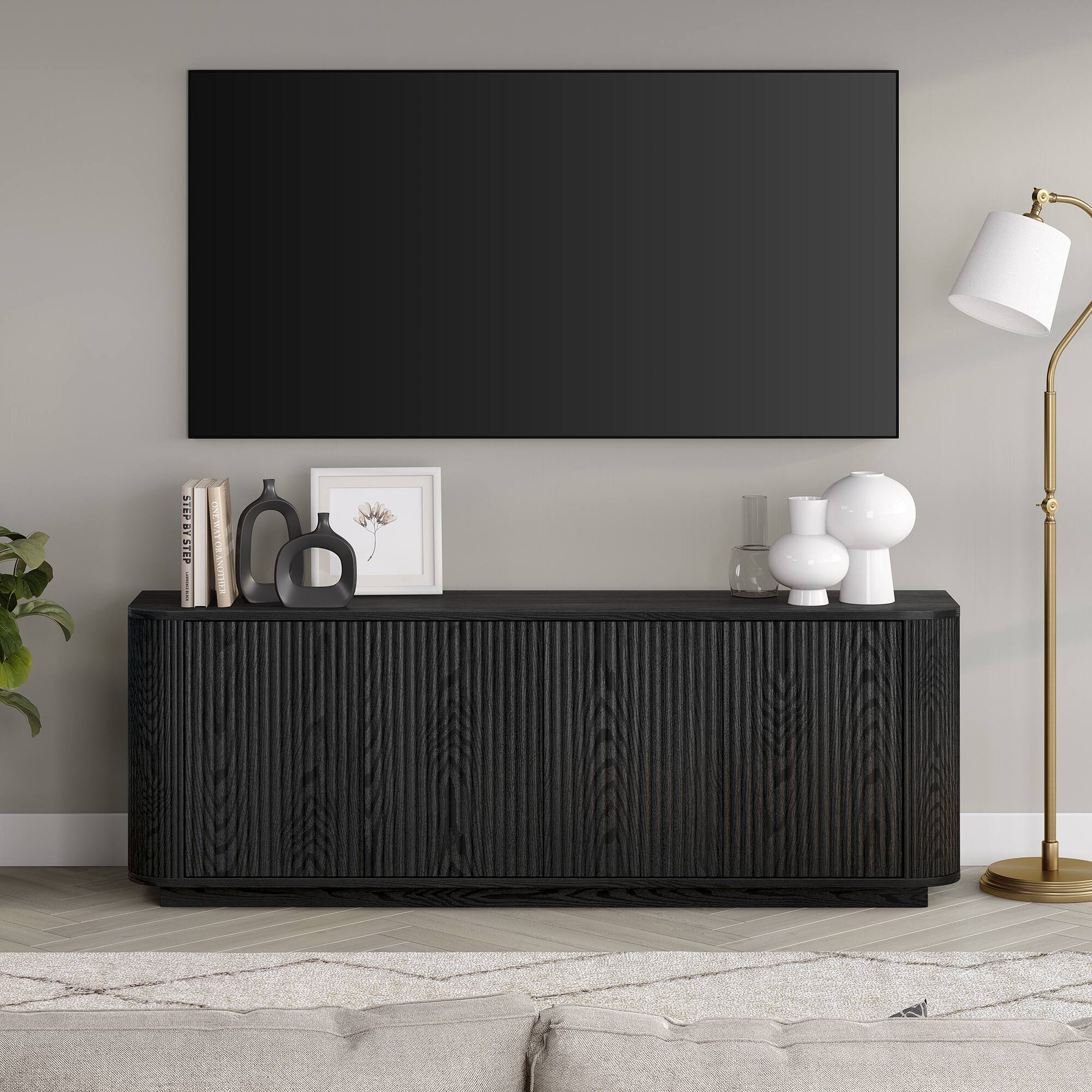 I cannot group or correct the text as it does not seem to be related to the image. The image shows a living room with a large flat screen TV mounted on the wall, a black table with a lamp and a vase, and a potted plant. There is also a book on the table.