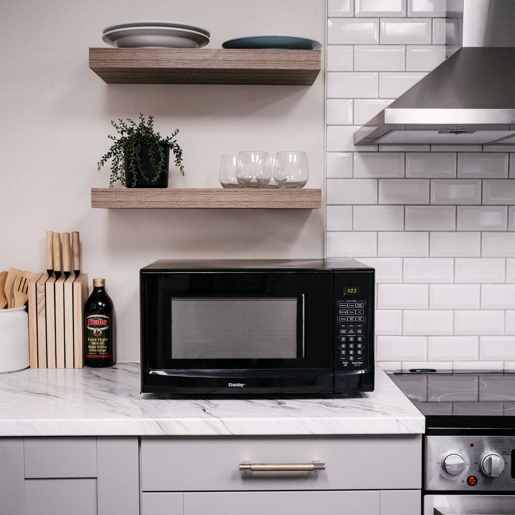 The image features a kitchen with a microwave on a marble countertop. The microwave is placed on a shelf, and there are several cups and bowls nearby. The kitchen also has a stove and a sink, making it a functional space for cooking and cleaning. The presence of a potted plant adds a touch of greenery to the room.