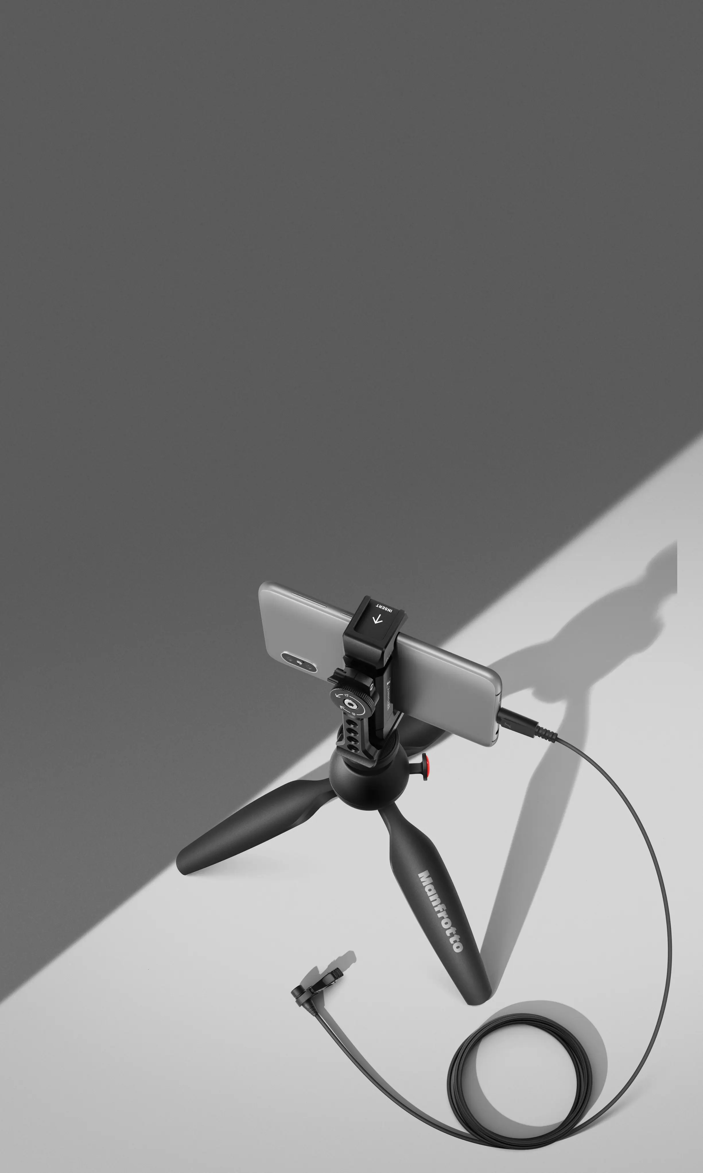 Manfrotto is a brand of camera equipment, including tripods and stands, that is known for its quality and durability. In the image, there is a Manfrotto tripod with a camera mounted on it, sitting on a white surface. The tripod is designed to provide stability and support for the camera, allowing photographers to capture images with ease and precision.