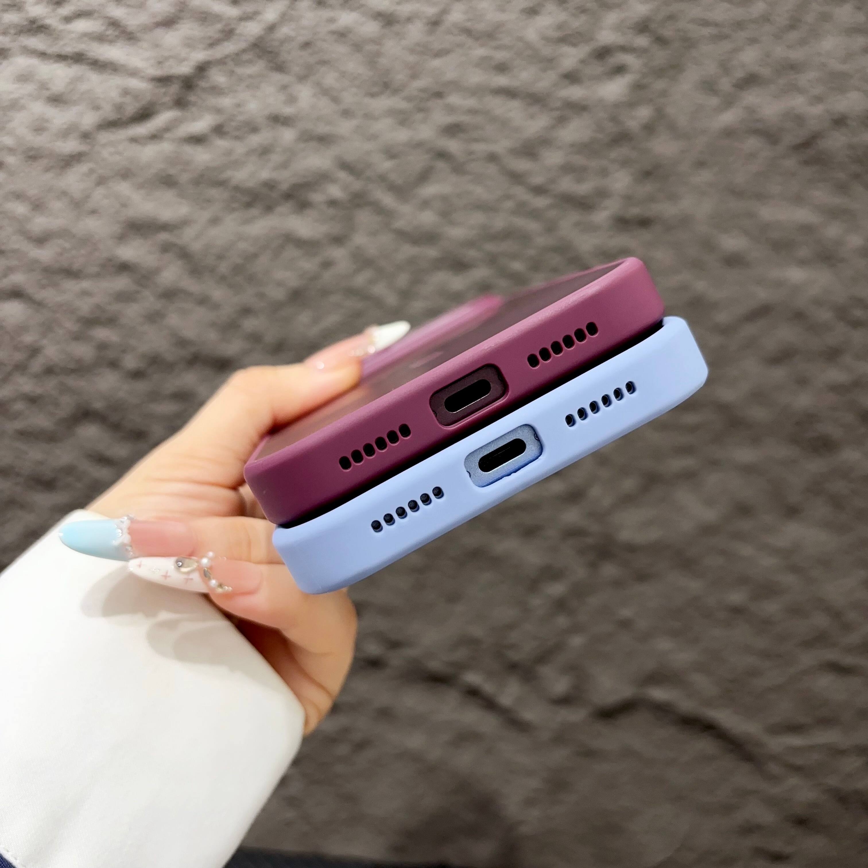 The image shows a close-up of a person's hand holding two smartphones, one purple and one blue, with their USB-C ports and speaker grills visible.