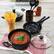 The image shows a kitchen scene with a pot of spaghetti sauce garnished with herbs, a pot of uncooked spaghetti, a jar of sauce, and cooking utensils on a wooden table.