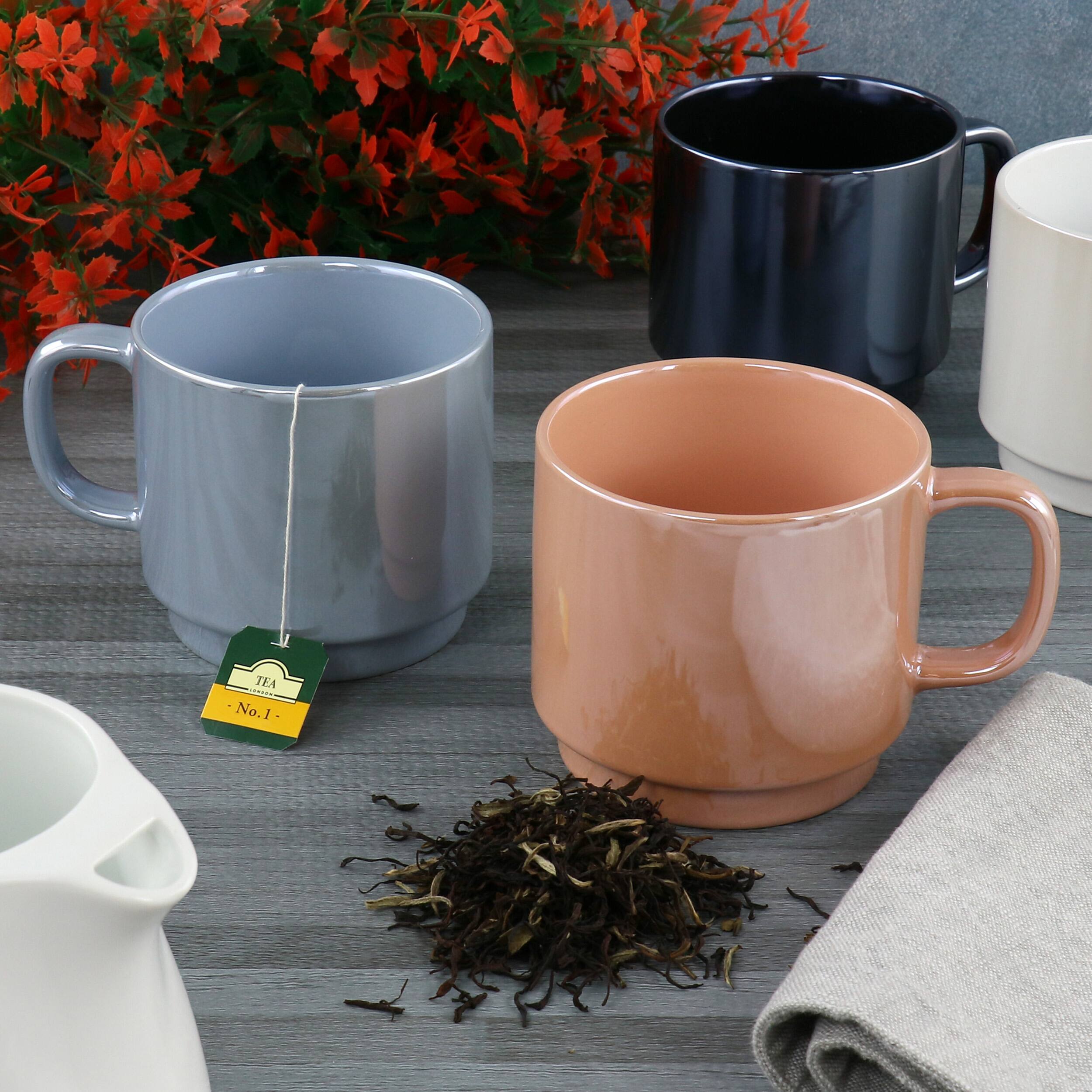 The image features a table with a variety of cups and a vase. There are four cups in total, with one being a pink coffee mug, and the others being blue coffee mugs. Additionally, there is a vase on the table, and a tea bag is placed on the table as well. The table is set up to serve tea, and the cups are ready for use.