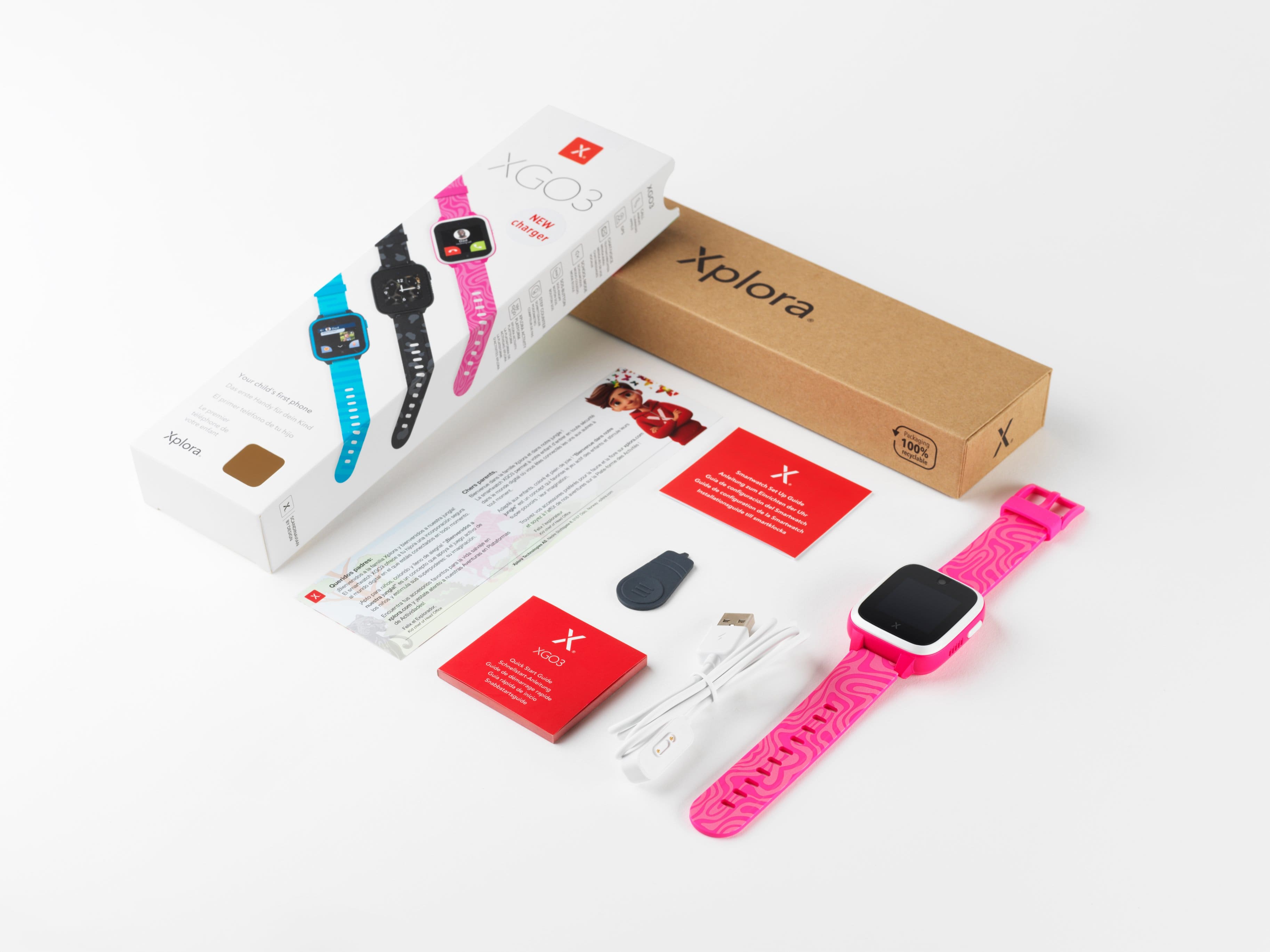 The image features a box containing a watch and a charger. The watch is pink and has a pink band. The box also contains a pamphlet and a card. The watch is displayed on a white background, making it the main focus of the image.