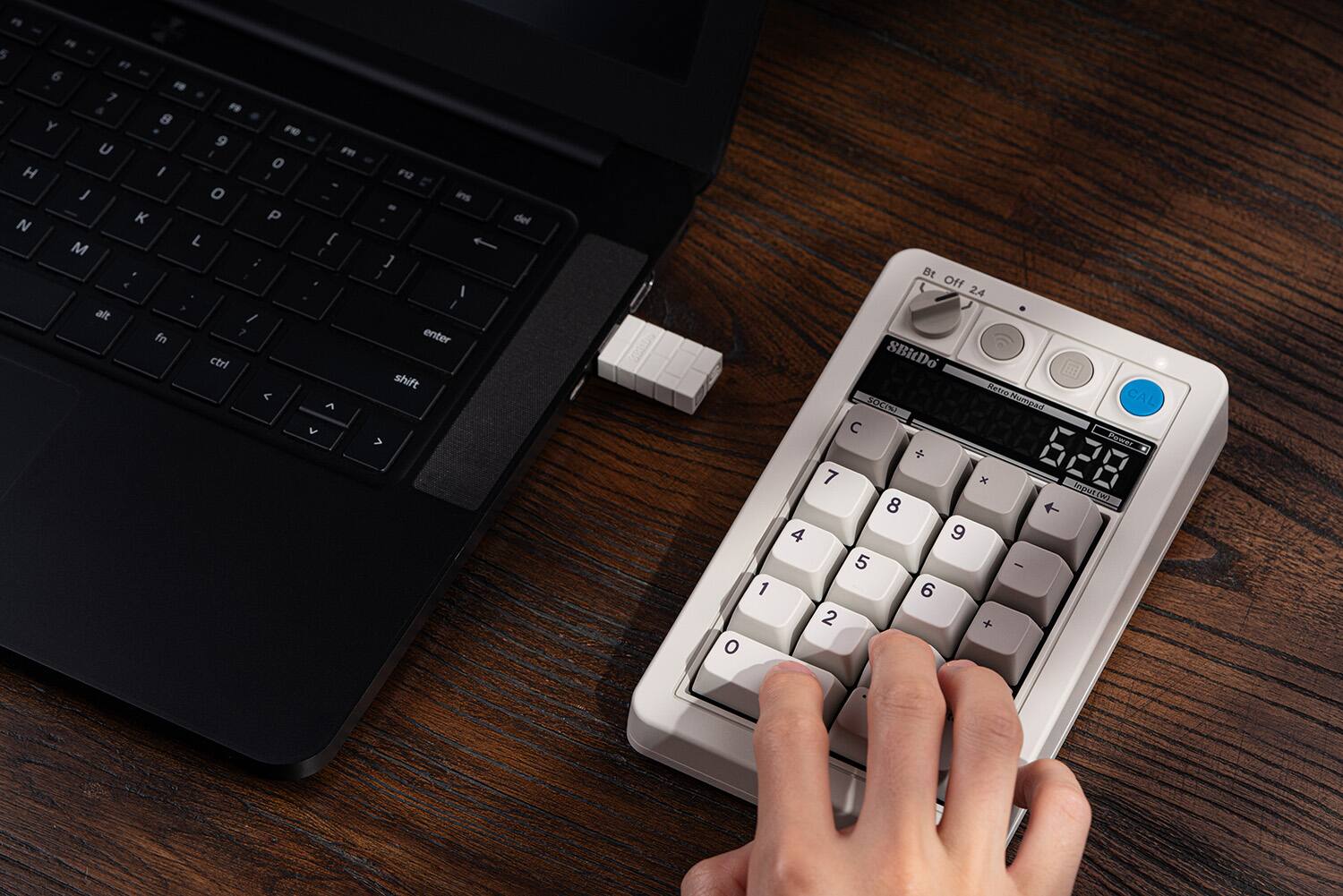 The image shows a person using a calculator and a laptop computer. The calculator is placed on the laptop, and the person is typing on the keyboard. The text on the image reads: "P 5 6 F 7 F Y 8 FD 9 U I F o H I I J o K P N L [ M ( ; 1 < alt / fn 7 ctrl < A > F2 ins - ] } I 1 enter shift > del o 1 4 Bt L Off 24 SBIDo Retre CAL SOCN Kamen  Pamer + 628 7 x meatm 8 + 9 5 - 6 2 + A".