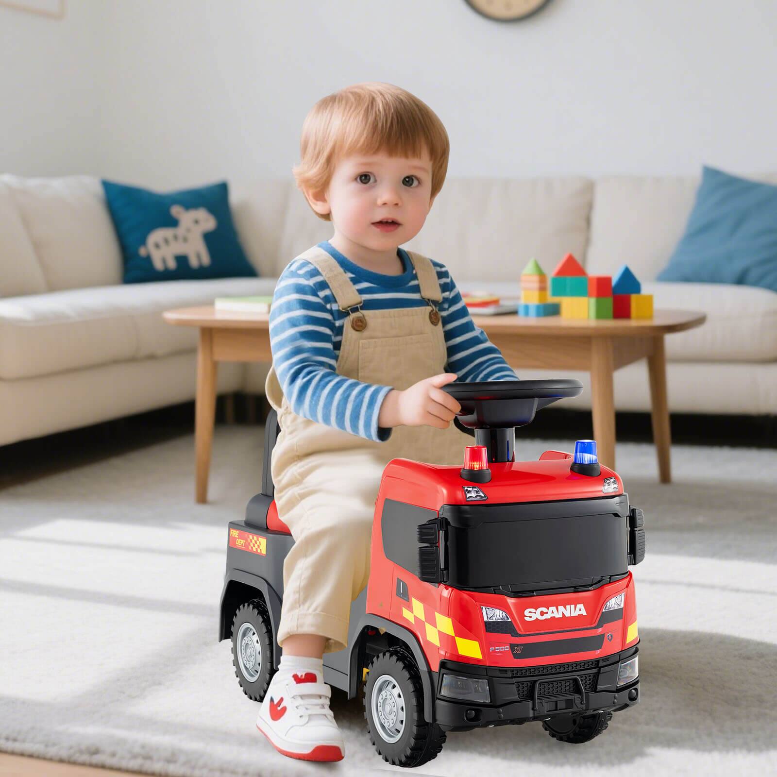 A toddler sits in a toy fire truck labeled "SCANIA" with the model "P200 2015."