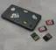 The image features a black laptop with various stickers on it, including one that says "New Game." The laptop is placed on a table, and around it, there are several small memory cards or game cartridges. The stickers on the laptop and the memory cards suggest that the laptop is used for gaming or other entertainment purposes.