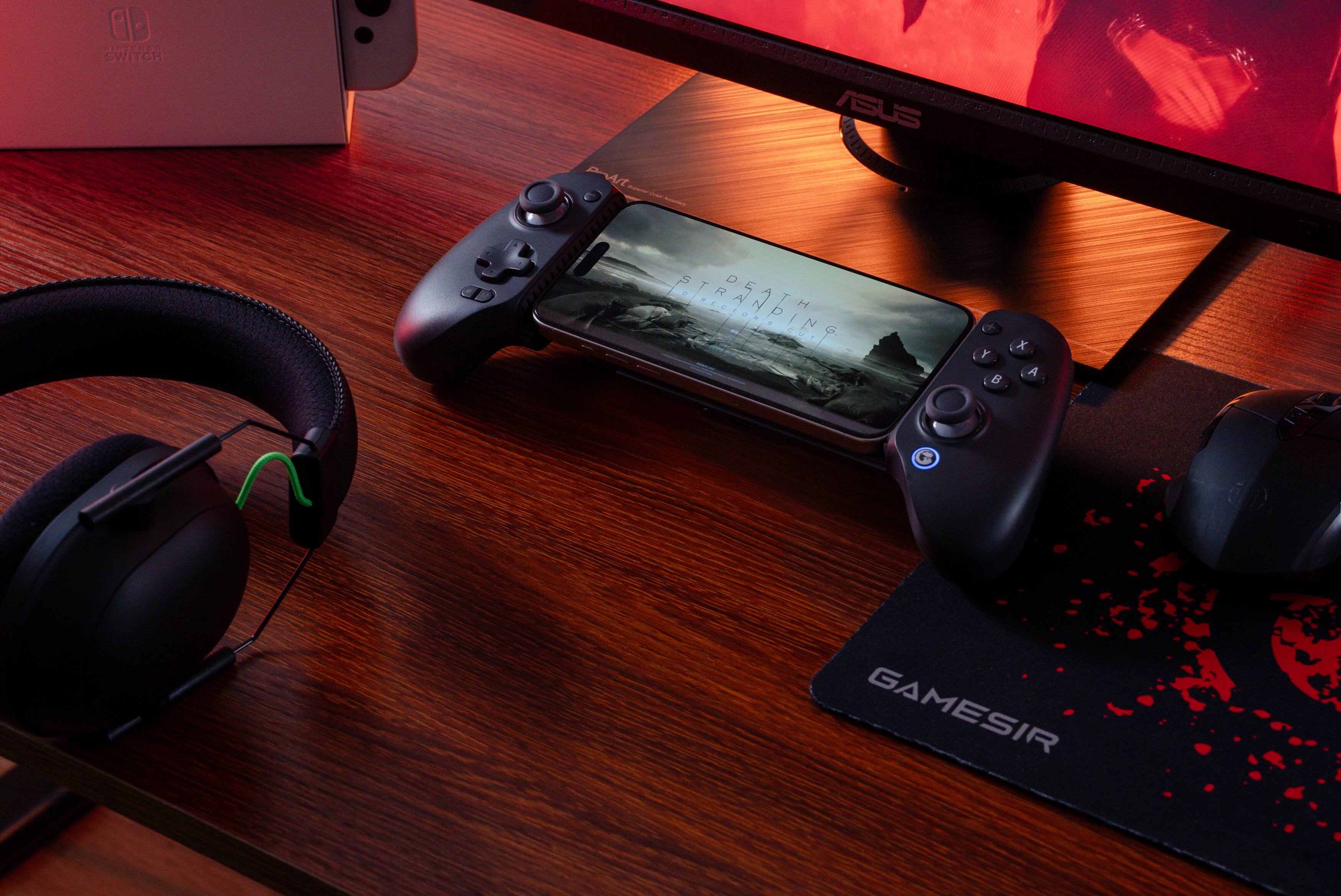 The image shows a wooden desk with a cell phone, two game controllers, and a pair of headphones. The cell phone is placed on top of the controllers, and the headphones are positioned on the left side of the desk. The scene suggests that someone is preparing to play a video game using the controllers and headphones.