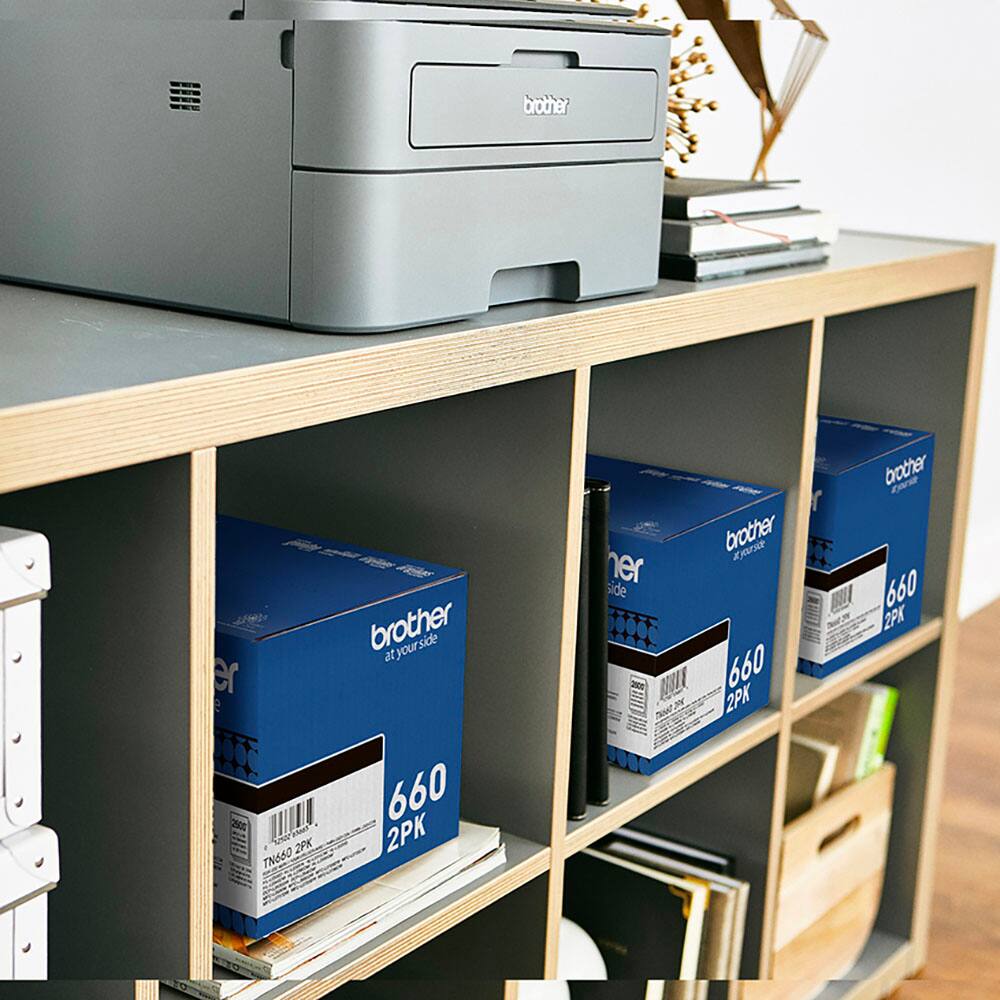 Brother printers are displayed on a shelf, with two boxes of Brother toner cartridges. The toner cartridges are labeled "660" and are available in 2-packs. The shelf also holds a book and a vase, adding to the overall organization and aesthetic of the space.