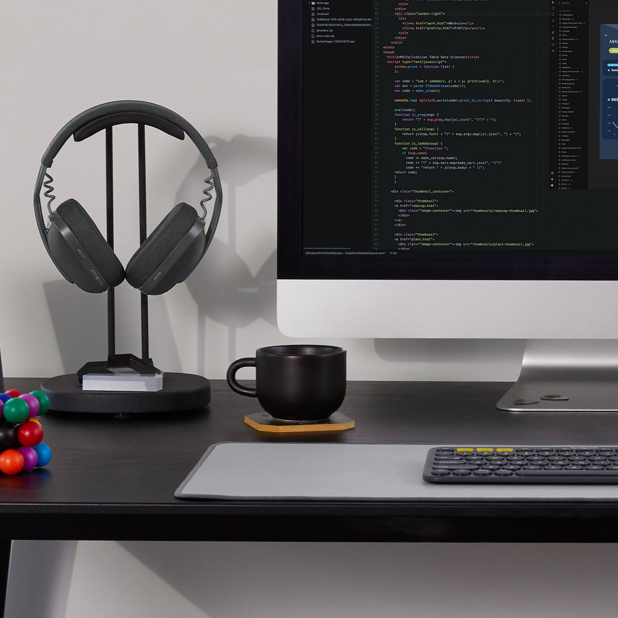 The image shows a computer desk with a monitor, keyboard, and mouse. The monitor displays a screen with a lot of text, which appears to be code. There is a coffee mug on the desk, and a pair of headphones can be seen nearby. The desk also has a pair of scissors and a calculator on it.