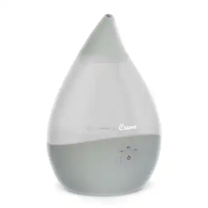 The image features a white Crane humidifier that is turned on. The humidifier is designed to provide a comfortable humidity level in the room, improving air quality and creating a more pleasant environment. The device is currently set to a low humidity setting, as indicated by the "LO" label on the front. The humidifier is sitting on a white surface, which further emphasizes its clean and minimalist design.