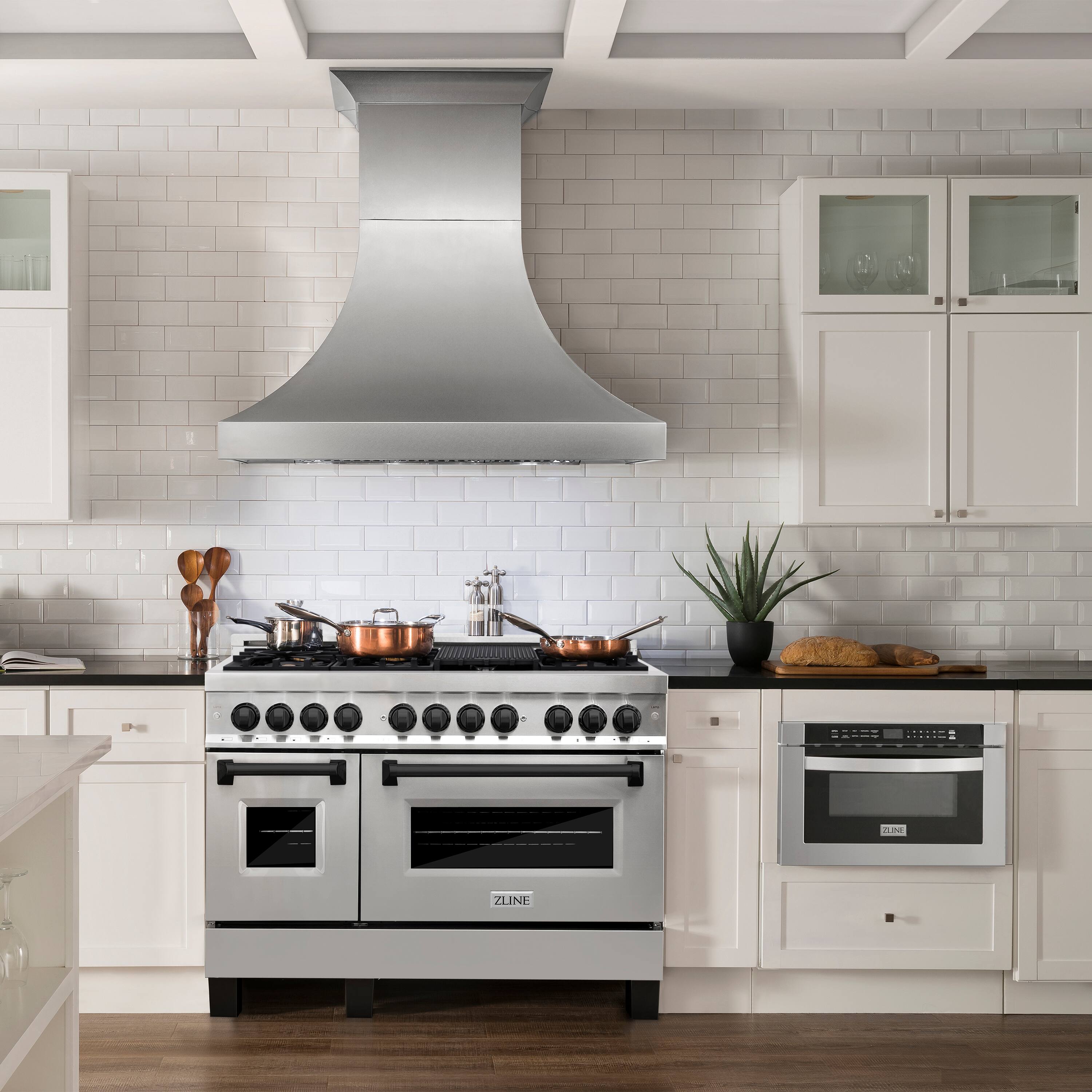 The image shows a kitchen with a stainless steel stove top oven and a vent hood. The oven is positioned under the vent hood, which is located above the stove. The kitchen also features white cabinets and a countertop. In addition to the stove, there is a potted plant and a knife block on the countertop. The kitchen appears to be well-equipped and ready for cooking.