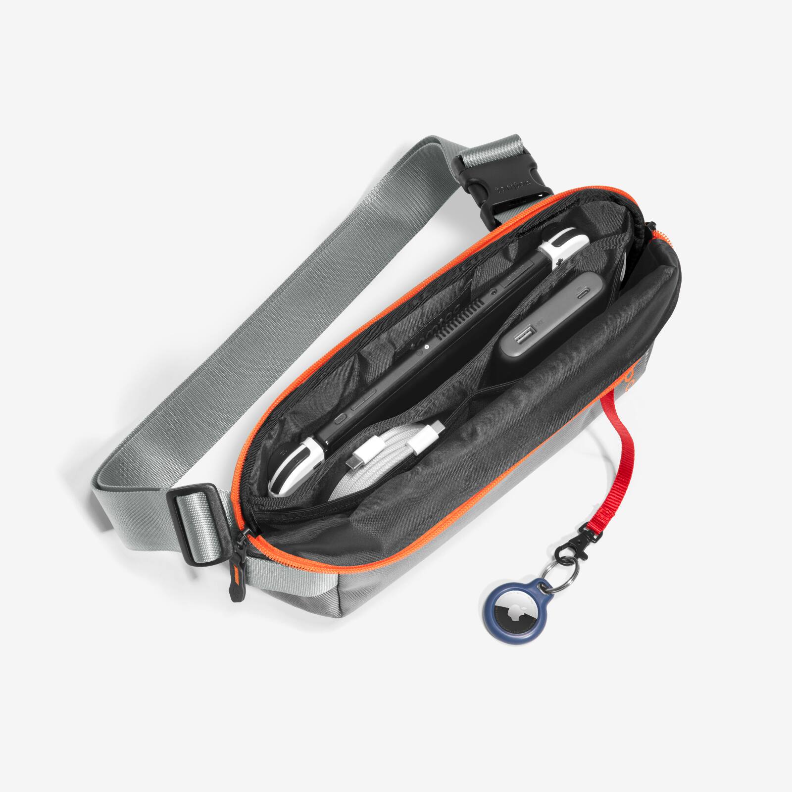 The image features a black and gray case with a red strap, which is open and empty. There is a small blue object, possibly a flash drive, lying next to the case. The case appears to be designed for carrying electronic devices, such as a laptop or a cell phone.