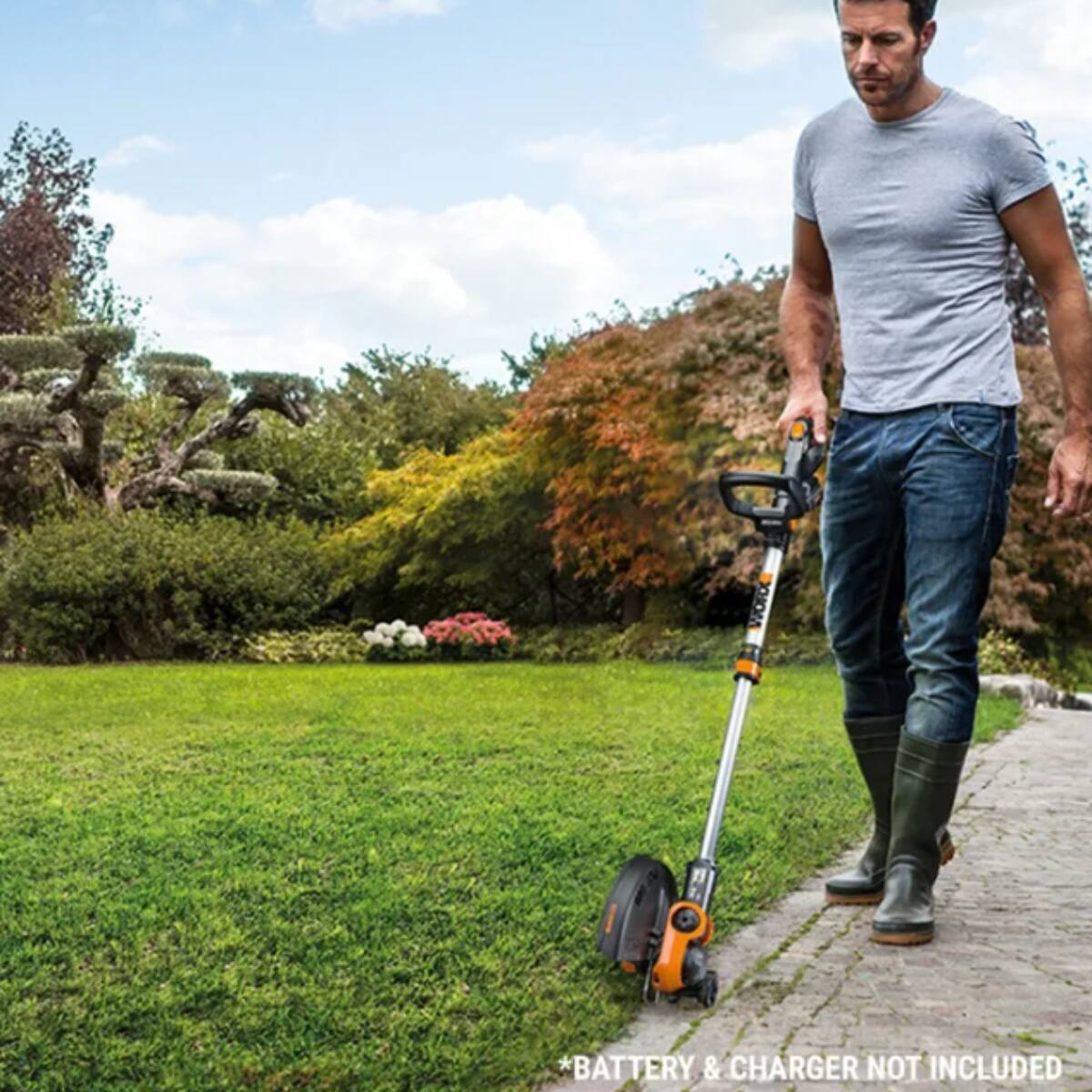 The image features a man standing in a grassy field, holding a cordless electric grass trimmer. The man is wearing a grey shirt and jeans, and he appears to be focused on his task. The grass trimmer is an essential tool for maintaining the yard, and the man seems to be using it effectively. The image also includes a cat in the background, adding a touch of liveliness to the scene.