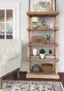 The image features a white couch placed next to a wooden bookshelf. The bookshelf is filled with various items, including books, vases, and a potted plant. There are three vases on the shelf, with one on the left side, one in the middle, and another on the right side. The potted plant is located on the right side of the bookshelf. The couch is situated on the left side of the bookshelf, creating a cozy and inviting atmosphere in the room.