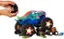 There is no text on the image. The image shows a person holding a toy car, specifically a monster truck, and placing it on top of a toy car.