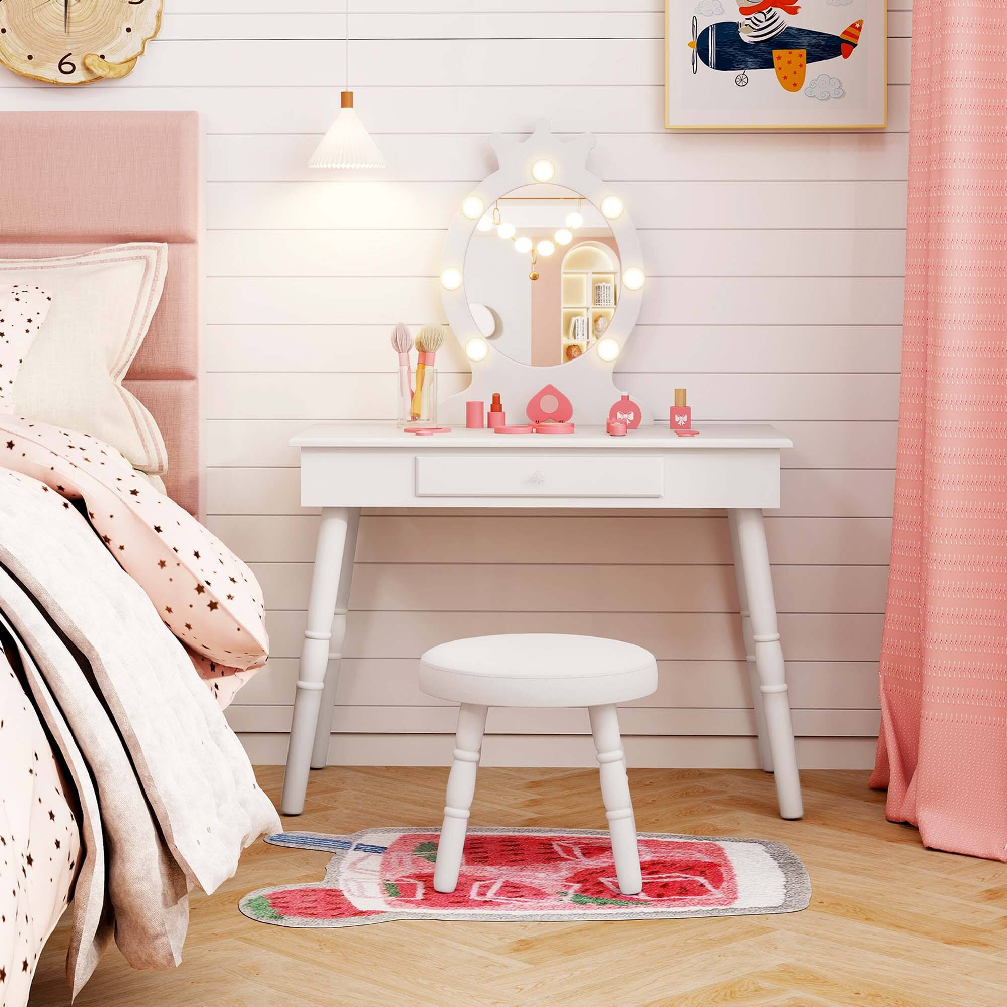 The image shows a cozy bedroom setup with a white vanity table and stool. The vanity table is adorned with a round mirror surrounded by lights, and various beauty products are placed on it. The stool is positioned on a red and white patterned rug. The room has a light wooden floor and a pastel-colored wall with horizontal paneling. A bed with a pink headboard and star-patterned bedding is partially visible on the left. A clock showing the time as 6 is mounted on the wall, and a painting of a whale is hung above the vanity. The room is softly lit, creating a serene atmosphere.