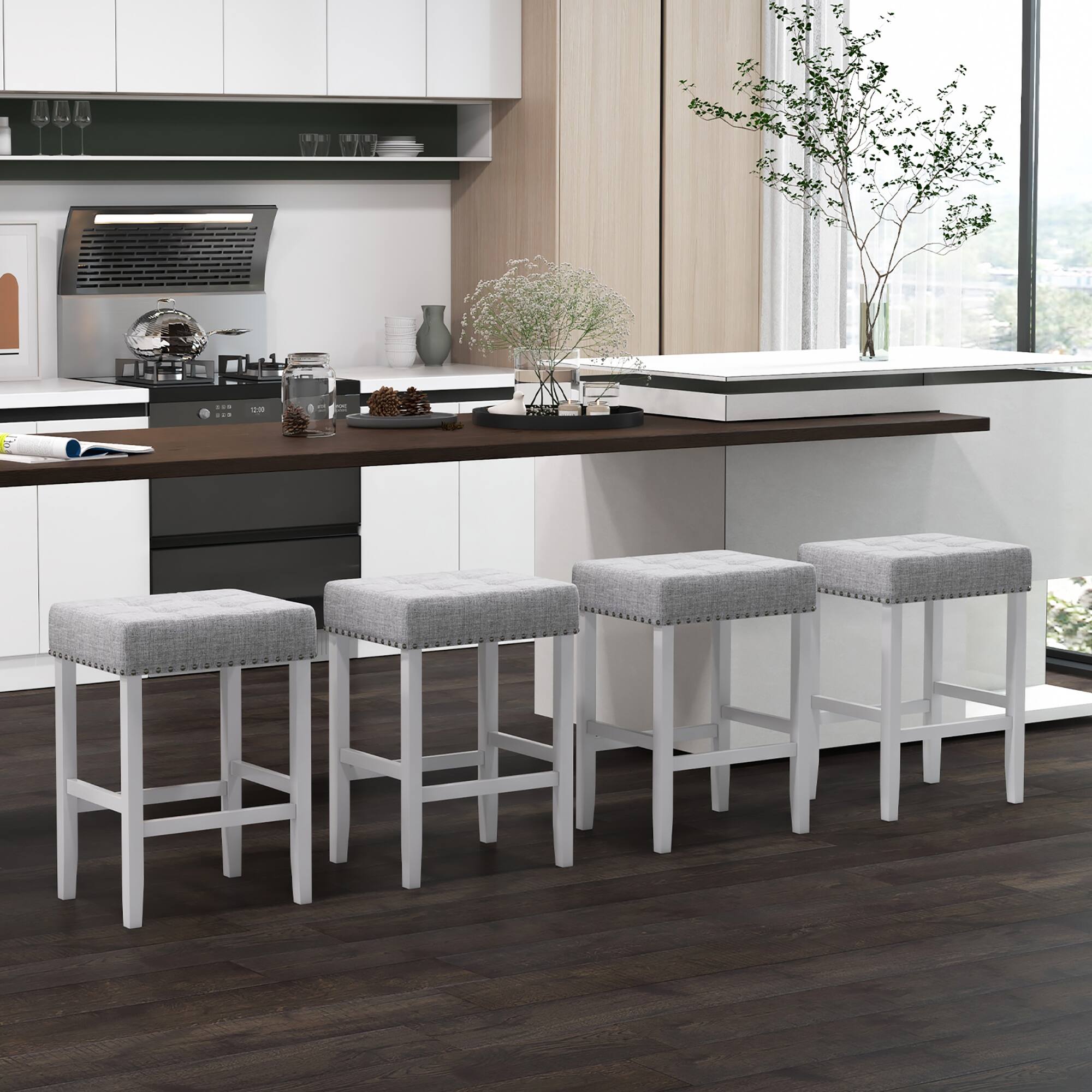 The image features a kitchen with a white countertop and a wooden floor. The kitchen is equipped with a sink, an oven, and a microwave. There are four white stools placed around the kitchen island, providing a comfortable seating area. 

In addition to the stools, there are several cups and a bowl on the countertop. A potted plant is also present in the kitchen, adding a touch of greenery to the space. The overall atmosphere of the kitchen appears clean and organized, making it an inviting and functional space for cooking and dining.