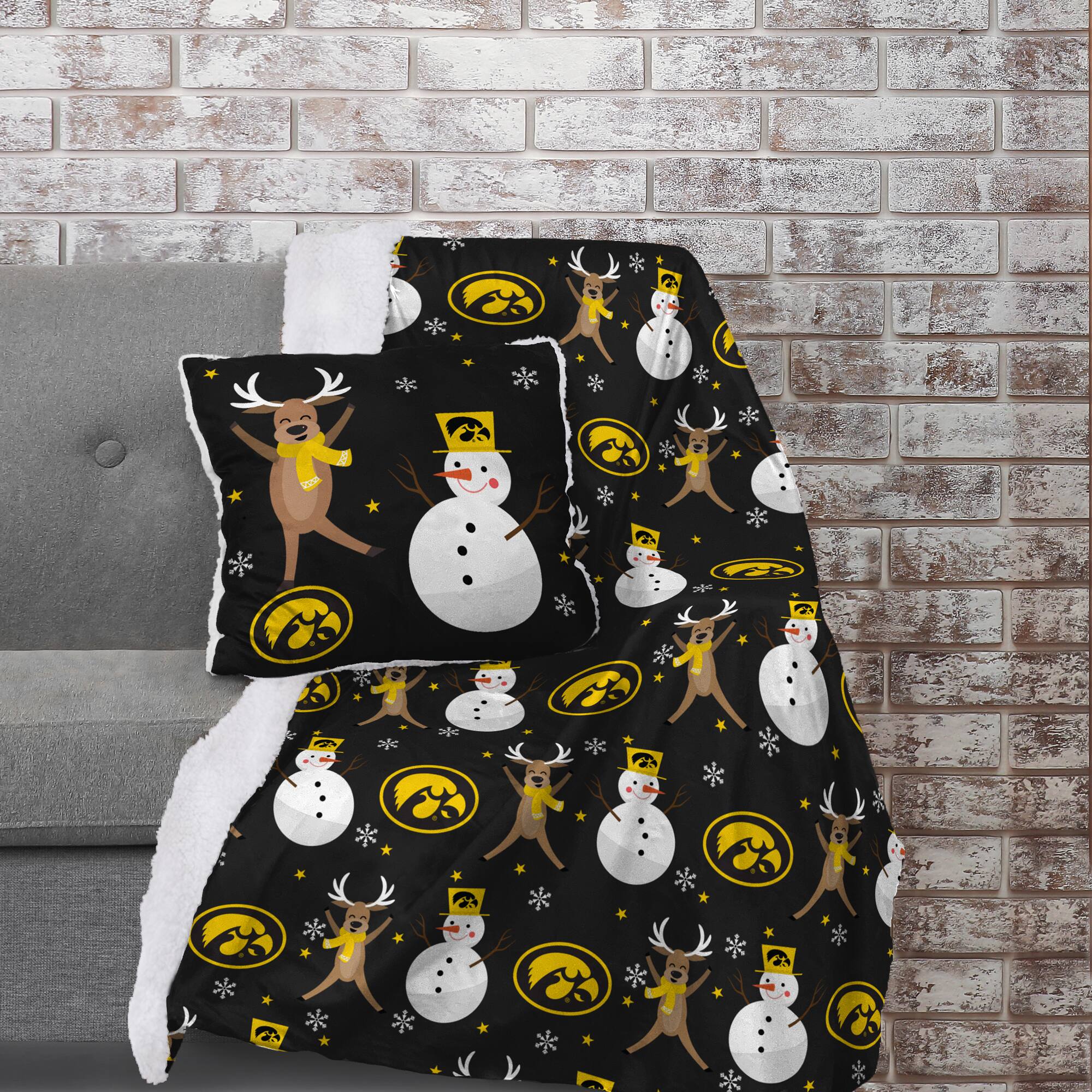 The image does not contain any text to group or correct. It shows a blanket and pillow with a festive design featuring reindeer, snowmen, and a logo.