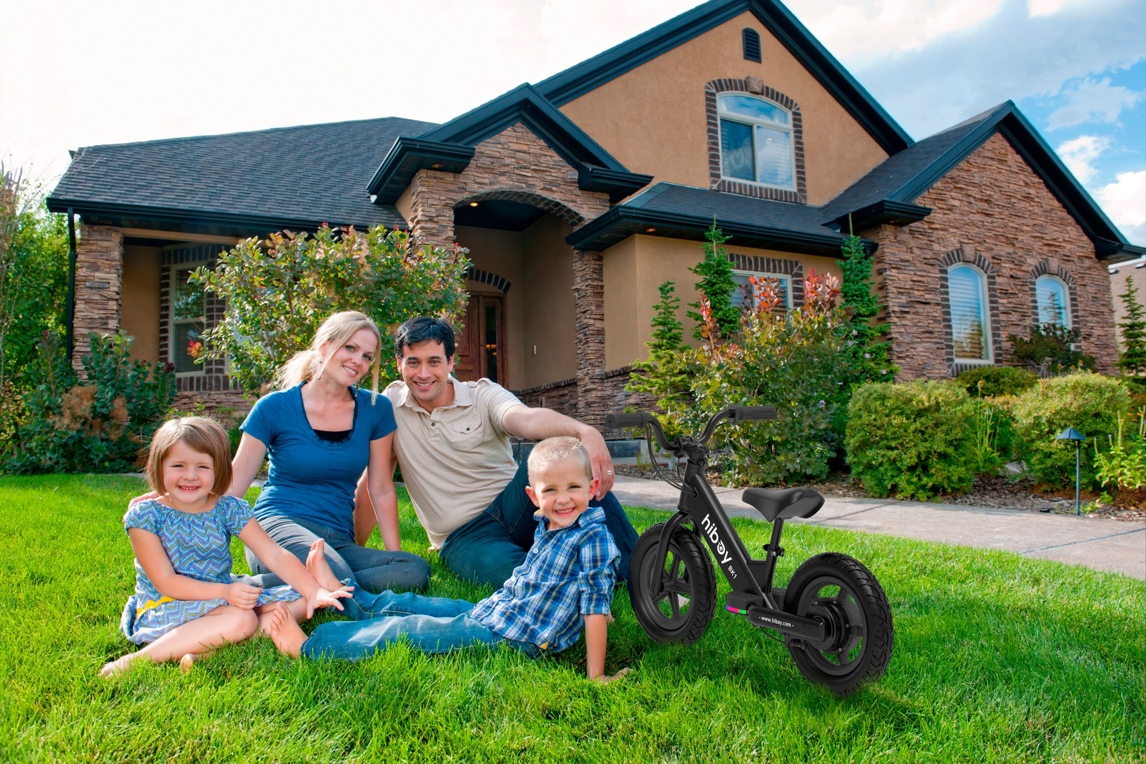 The image shows a family of four sitting on the grass in front of a house. The family consists of a man, a woman, and two children. They are posing for a picture, and there is a motorcycle parked nearby. The family appears to be enjoying their time together outdoors.