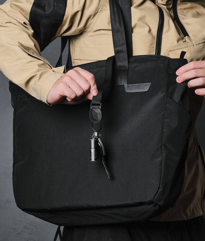 Left. ALPAKA - Metro Tote Laptop Tote Bag for Work, Work Tote Fits 16" MacBook Pro, Side Bottle Pocket, Weather-Resistant, Key Tether - Black Axoflux 210D.