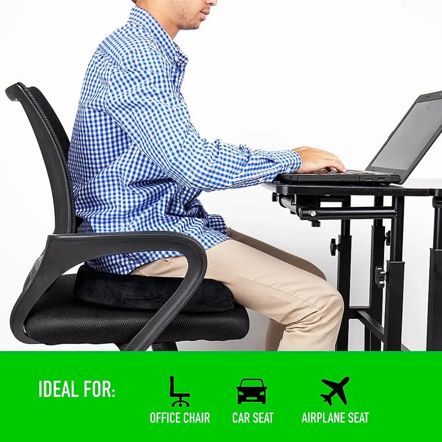 The image features a man sitting on a black office chair, working on a laptop placed on a desk. The man is wearing a blue shirt and appears to be focused on his work. The office chair is positioned in front of a dining table, which has a laptop on it. The scene suggests that the man is working in a comfortable and well-equipped workspace.