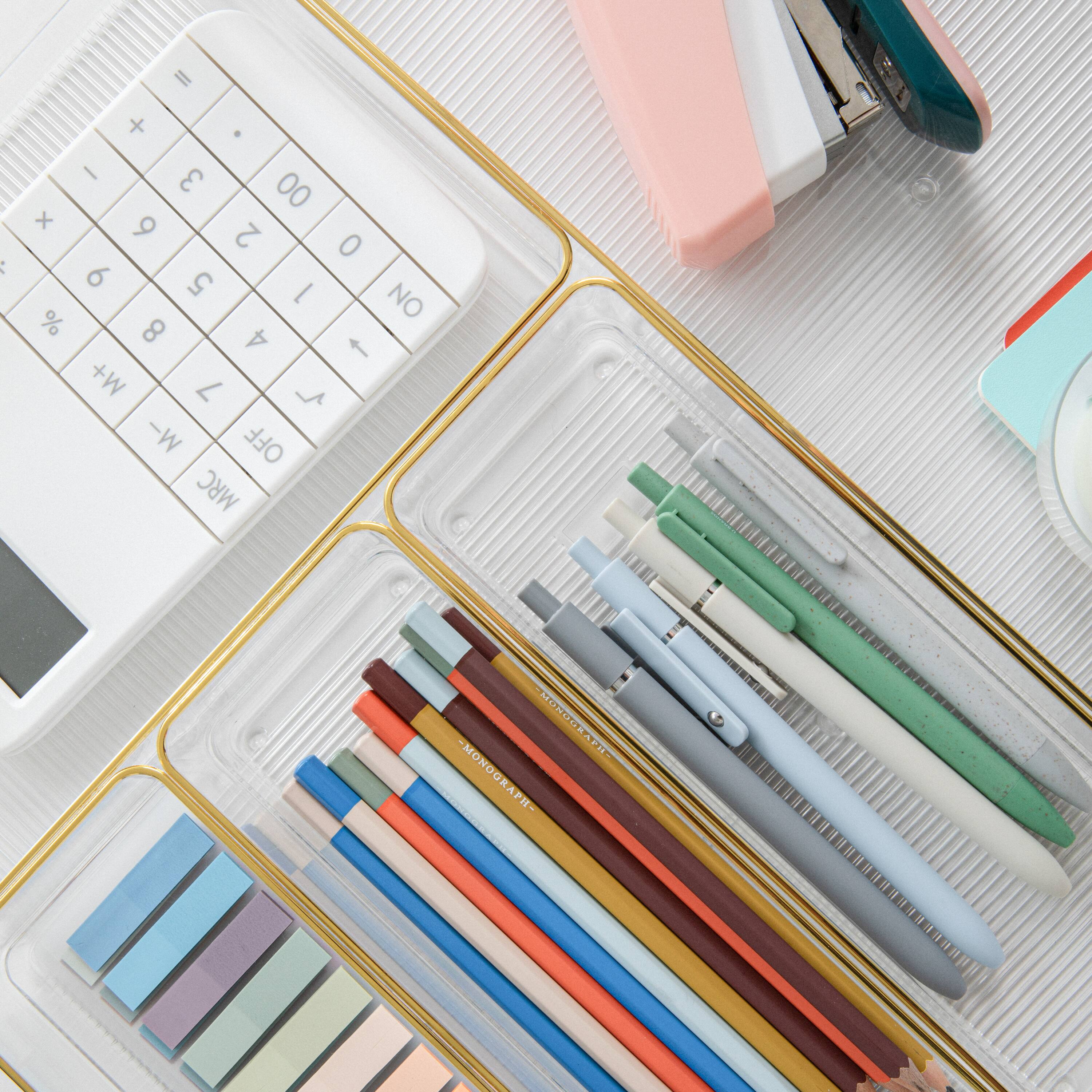 The image features a white calculator, a pink container, and a clear container with various pens and pencils. The calculator has a white and black color scheme, and it is placed next to the pink container. The clear container holds pens and pencils, with a total of 12 pens and 1 pencil. The pens are of different colors and sizes, and they are neatly organized within the container. The calculator is a prominent feature in the image, and the pens and pencils in the clear container add a touch of organization and functionality to the scene.