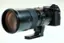 The image features a large camera lens, which is a part of a camera. The lens is black and has a large aperture, making it suitable for capturing high-quality images. The lens is mounted on a camera, and it is placed on a white background. The lens is designed for use with the Fujifilm GFX 100s camera, providing excellent performance and image quality.