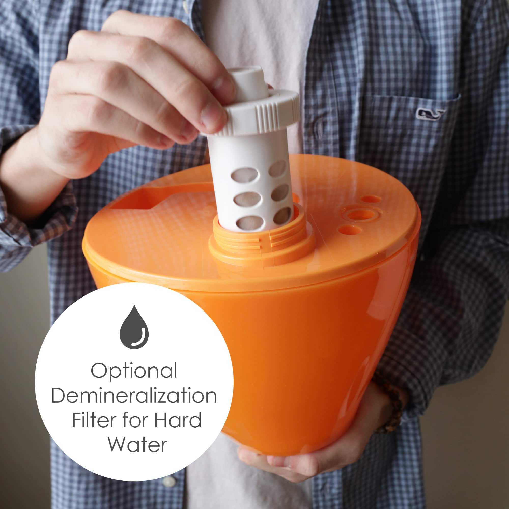 The image shows a person holding an orange container with a white lid, which is a water filter. The person is pouring water into the container. The text "Optional Demineralization Filter for Hard Water" is displayed in the bottom left corner of the image.