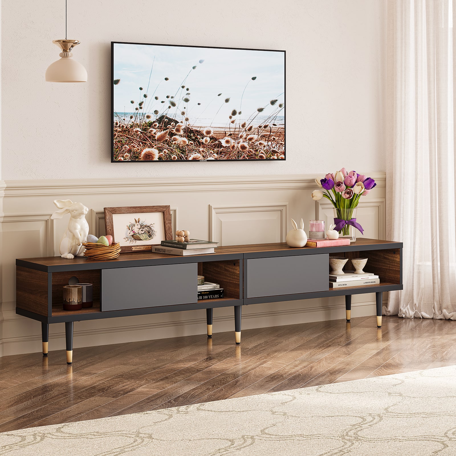 The image features a living room with a wooden entertainment center. On the entertainment center, there is a flat screen TV mounted on the wall. Above the entertainment center, there is a large picture hanging on the wall. The room also includes a table with a vase of flowers and a book on it. The table is placed in front of the entertainment center, and there is a bowl nearby. The living room is decorated with a rug, and the overall atmosphere is cozy and inviting.