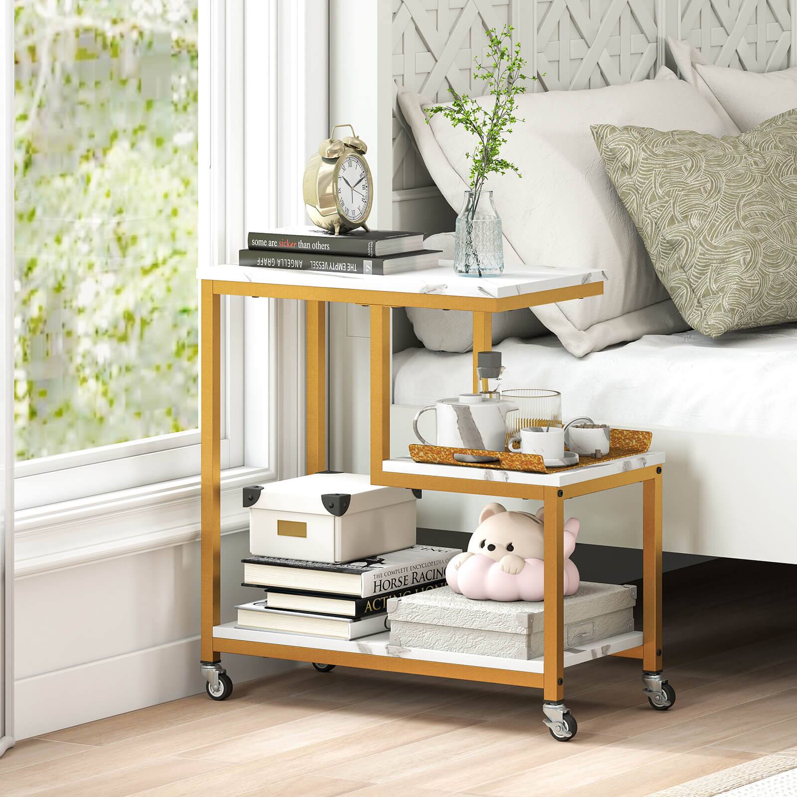 The image features a small cart with a clock on top of it, placed next to a bed. The cart is filled with various items, including books, a cup, and a vase. There is also a teddy bear on the cart, adding a touch of warmth and comfort to the scene. The cart is positioned near a window, which allows natural light to illuminate the space. The arrangement of the items on the cart suggests a cozy and organized living environment.