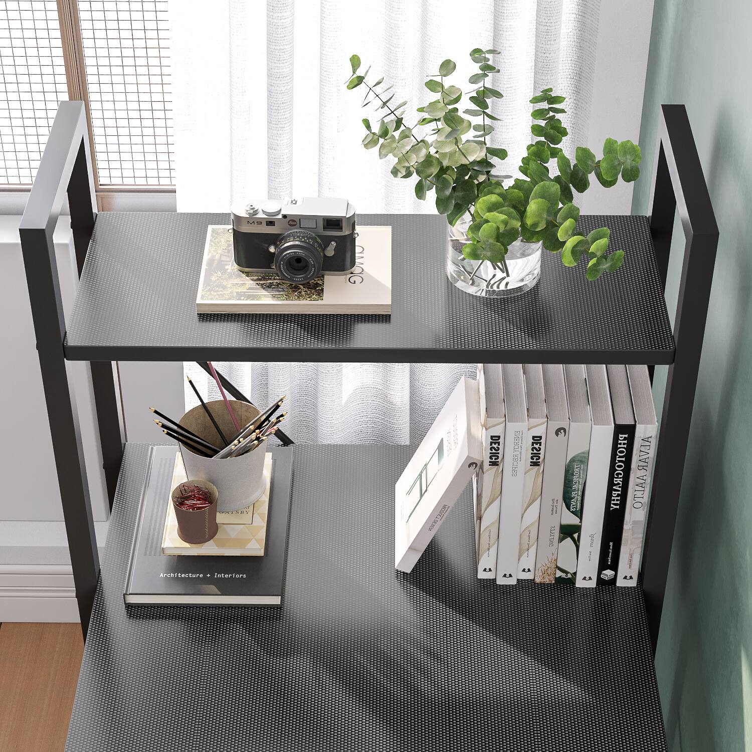 The image features a black shelf with various items on it. There are several books placed on the shelf, including a book titled "Alvar Aalto." Additionally, there is a vase with plants in it, a camera, and a cup. The shelf is located near a window, providing natural light to the space.