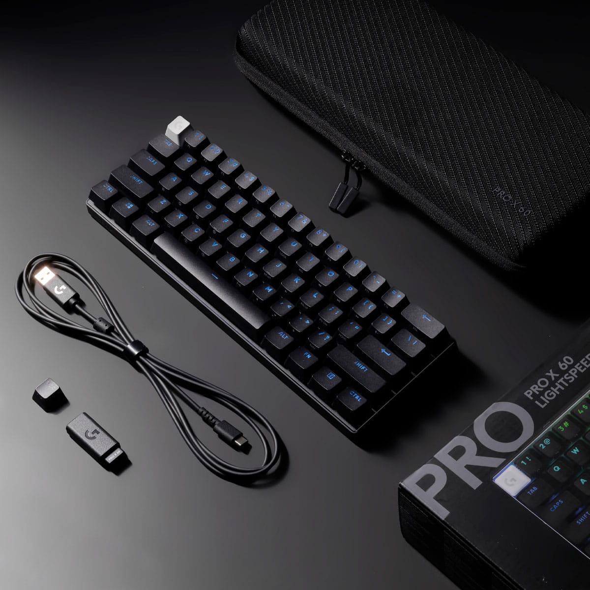 The image features a black keyboard with blue keys, a black case, and a black cord. The keyboard is placed on a black surface, and there is a small box next to it. The keyboard is connected to a computer, and the case is likely used for carrying the keyboard and other accessories. The overall setup suggests a portable and convenient workspace for the user.