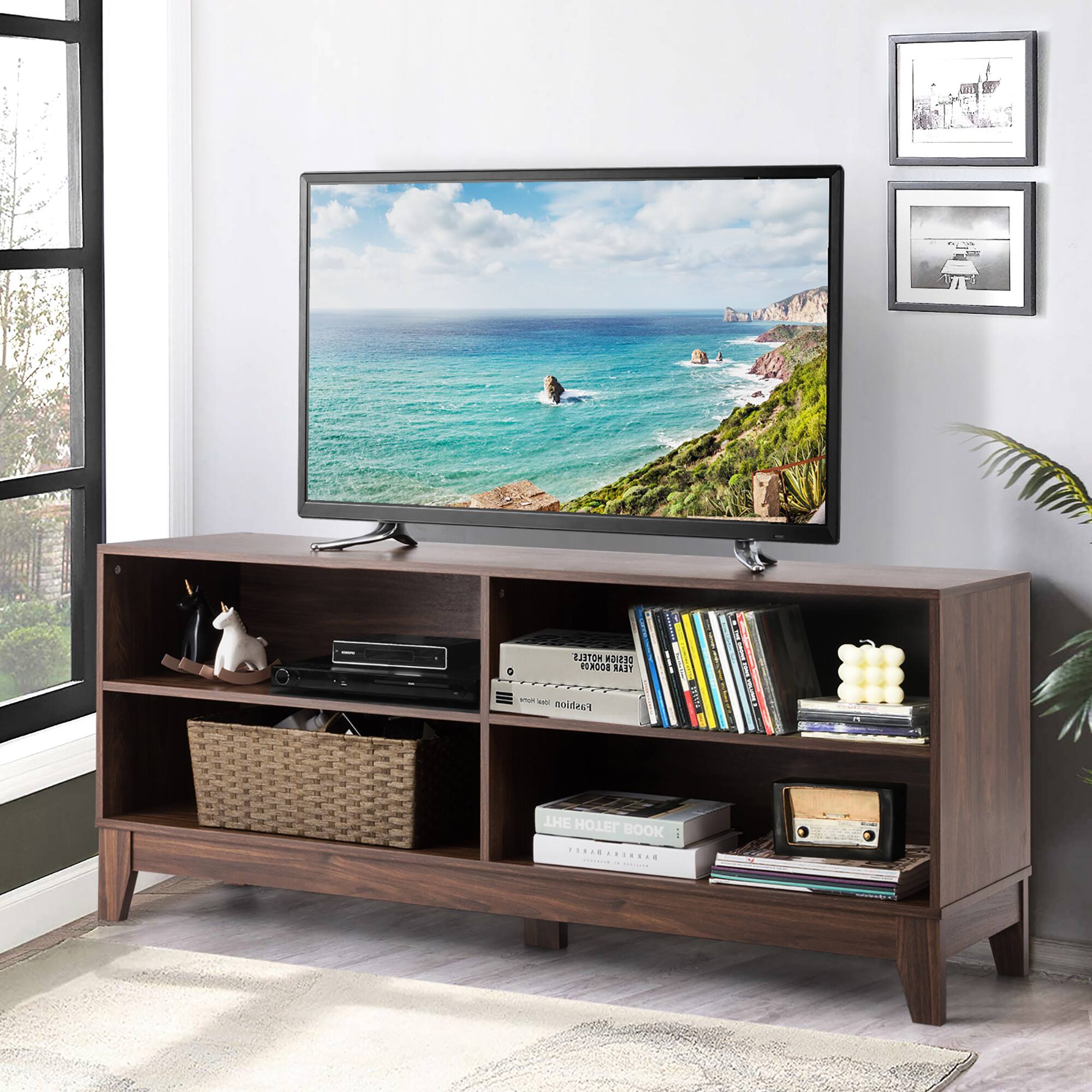 The image shows a television sitting on top of a wooden stand in a room. The television is displaying a picture of the ocean, and the stand is filled with various items such as books and a remote control. The room also features a window, and there is a potted plant nearby. The overall scene suggests a cozy and comfortable living space.