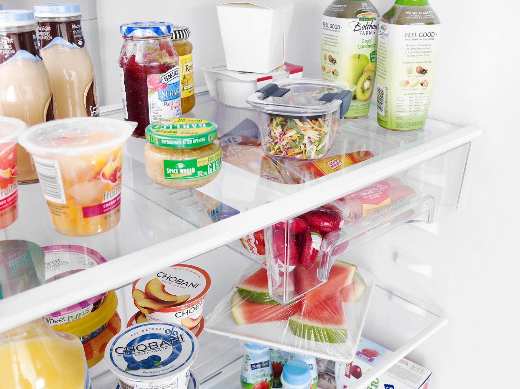 The refrigerator is filled with a variety of food items, including fruits, vegetables, and drinks. There are several bottles of juice, milk, and other beverages, as well as a bowl of fruit. The refrigerator also contains a variety of food items such as hummus, yogurt, and other snacks. The assortment of food and drinks suggests that the refrigerator is well-stocked and ready for use.