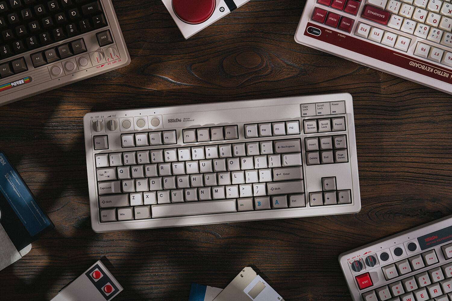 The image features a wooden table with a variety of keyboards and a book. The keyboards include a retro keyboard, a computer keyboard, and a keyboard with a red key. The book is located on the left side of the table. The arrangement of the keyboards and the book creates an interesting and unique display.