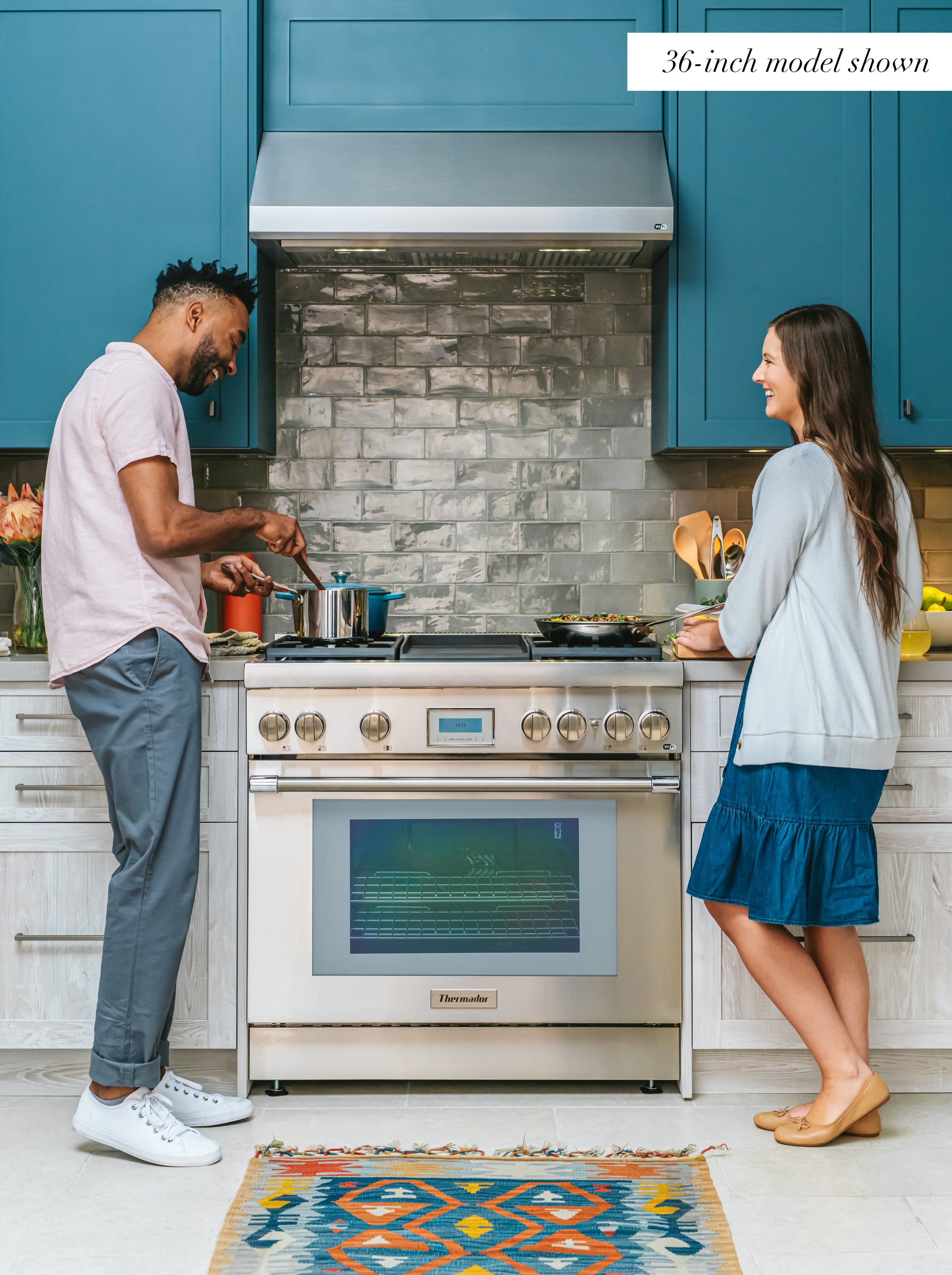 The image features a man and a woman standing in a kitchen, with the man wearing a pink shirt and the woman wearing a blue skirt. They are both smiling and appear to be enjoying their time together. The kitchen is equipped with a stove top oven, which is a 36-inch model. The oven is located in the middle of the kitchen, and the couple is standing on either side of it.