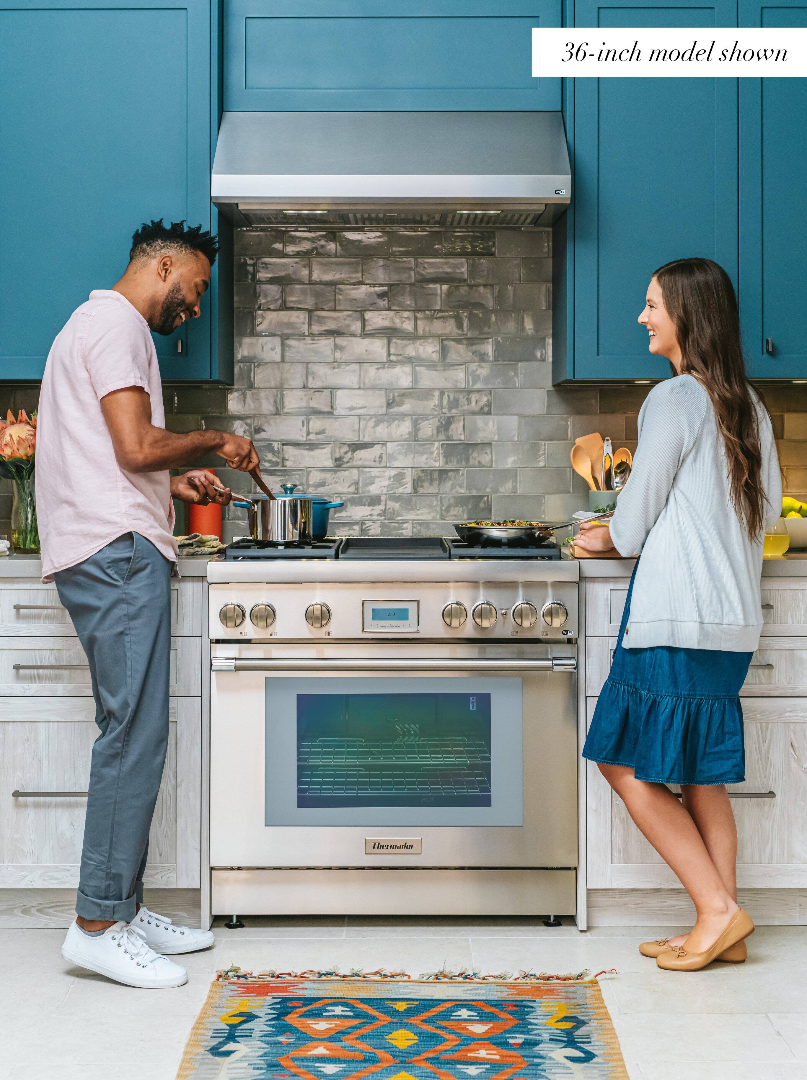 The image features a man and a woman standing in a kitchen, with the man wearing a pink shirt and the woman wearing a blue skirt. They are both smiling and appear to be enjoying their time together. The kitchen is equipped with a stove top oven, which is a 36-inch model. The oven is located in the middle of the kitchen, and the couple is standing on either side of it.