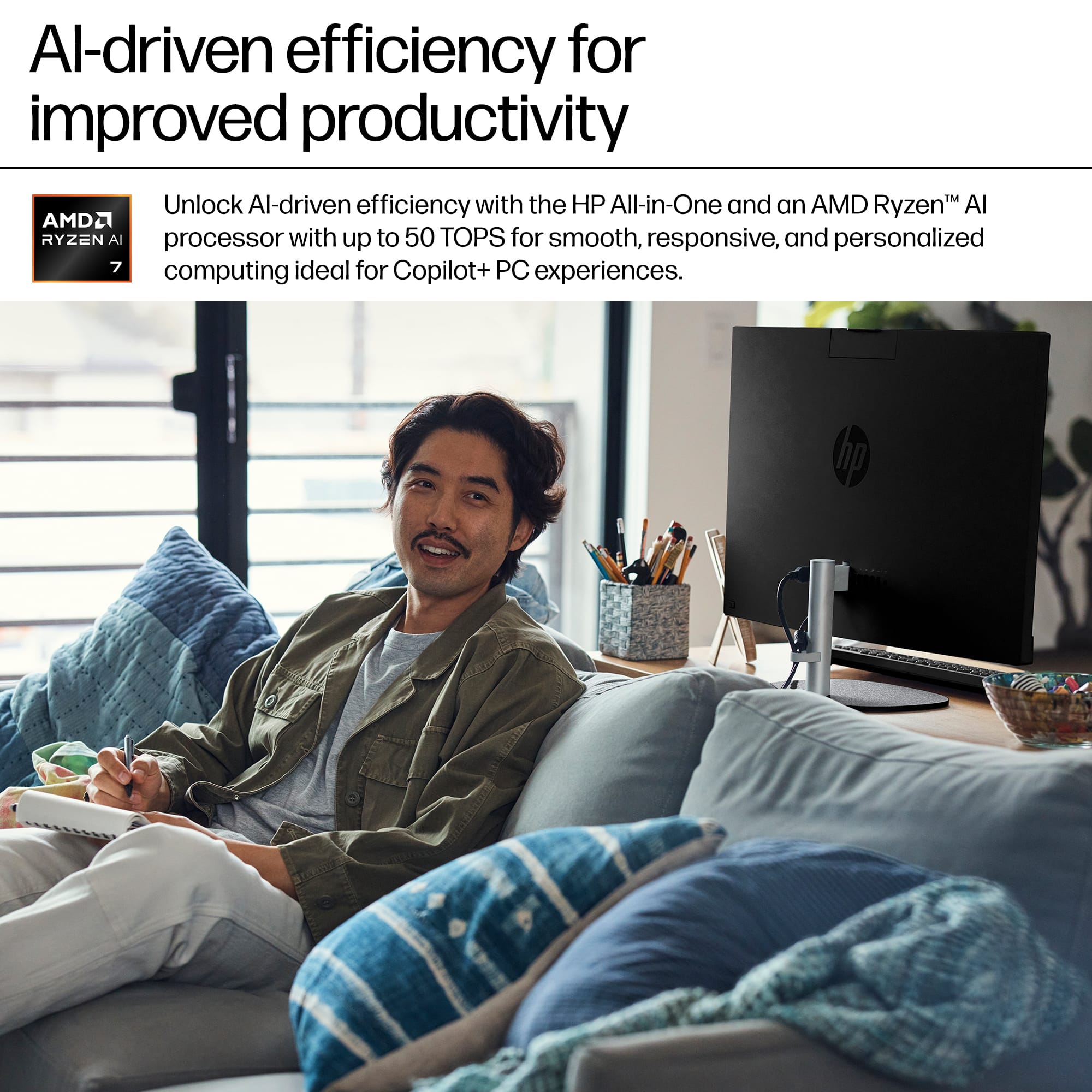 "Al-driven efficiency for improved productivity" is the main message of the image. The image features a man sitting on a couch with a laptop and a book, possibly working or studying. The laptop is an HP All-in-One with an AMD Ryzen Al processor, which is designed to provide up to 50 TOPS for smooth, responsive, and personalized computing experiences. The image suggests that using this laptop can enhance productivity and efficiency in various tasks, such as work or study.