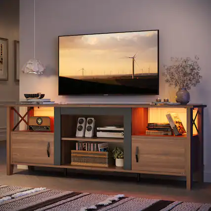 The image features a living room with a large flat screen TV mounted on the wall. The TV is displaying a picture of windmills. The room also has a wooden entertainment center with a speaker and a clock. There are several books scattered around the room, and a potted plant is placed nearby. Additionally, there is a vase and a bowl in the room, adding to the overall decor.