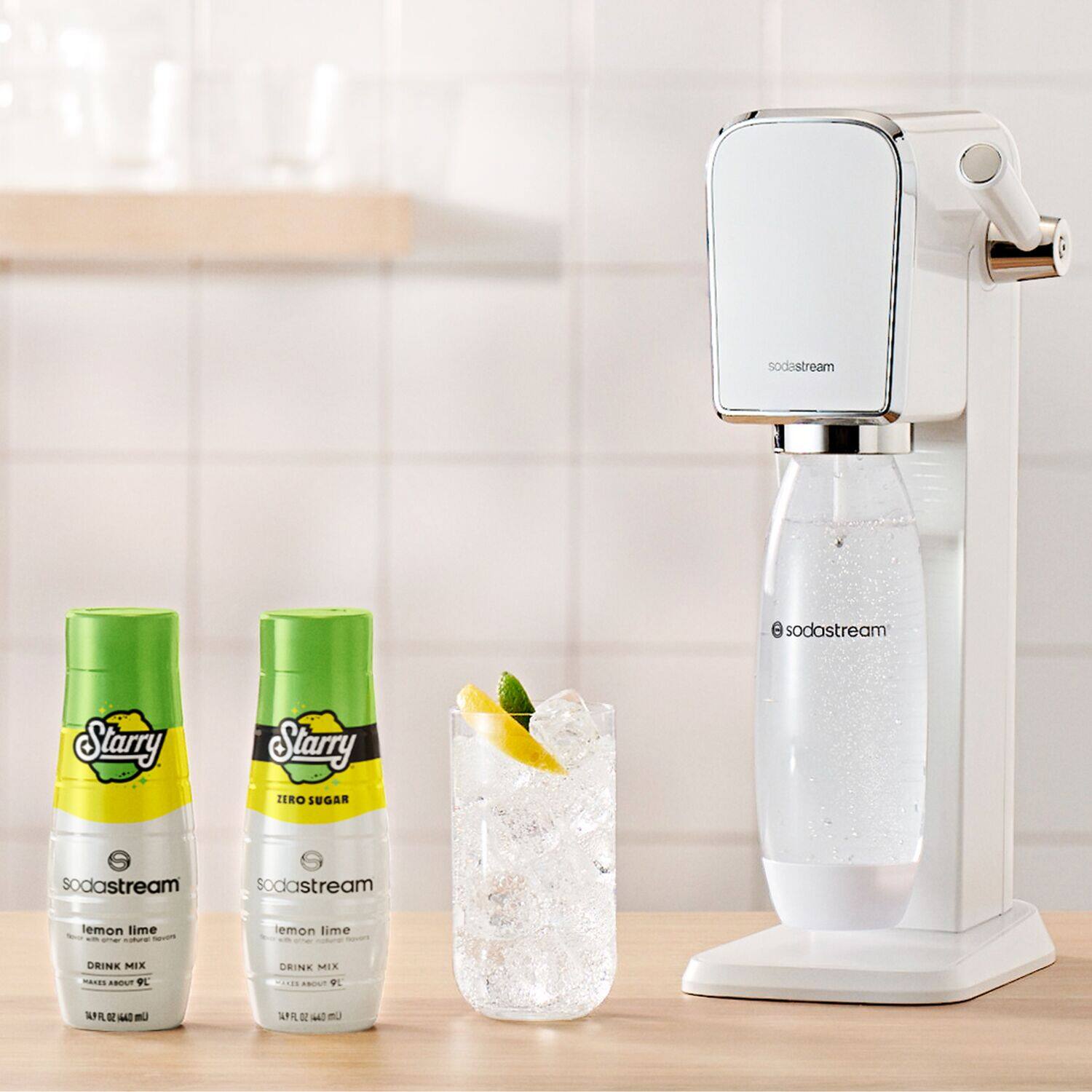 The image features a table with a SodaStream machine, a glass of lemon-lime soda, and three bottles of Starry Starry flavored syrups. The table is white, and the SodaStream machine is positioned on the right side of the table. The glass of soda is placed in the middle of the table, and the three bottles of Starry Starry flavored syrups are lined up on the left side of the table.