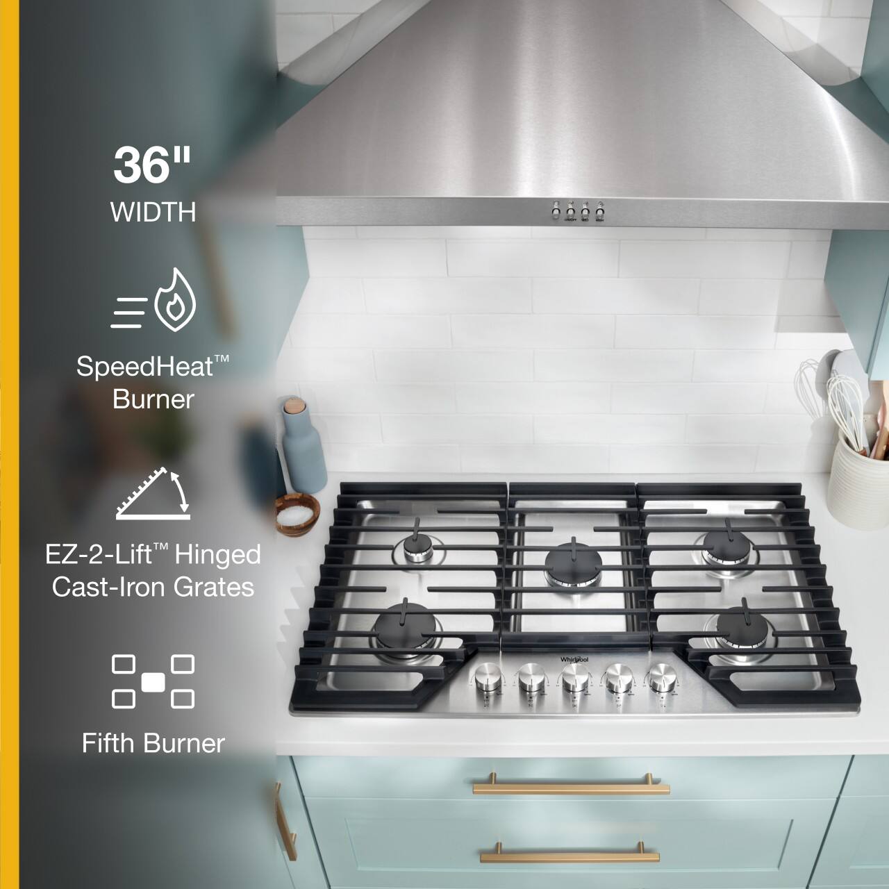 The image features a stove top with a 36" width, SpeedHeat Burner, EZ-2-Lift Hinged Cast-Iron Grates, and a Fifth Burner. The stove top is white, and the stove is positioned under a stainless steel hood. The stove is equipped with various cooking utensils, including a spoon and a knife, which are placed on the countertop. The overall scene showcases a well-equipped and functional kitchen space.