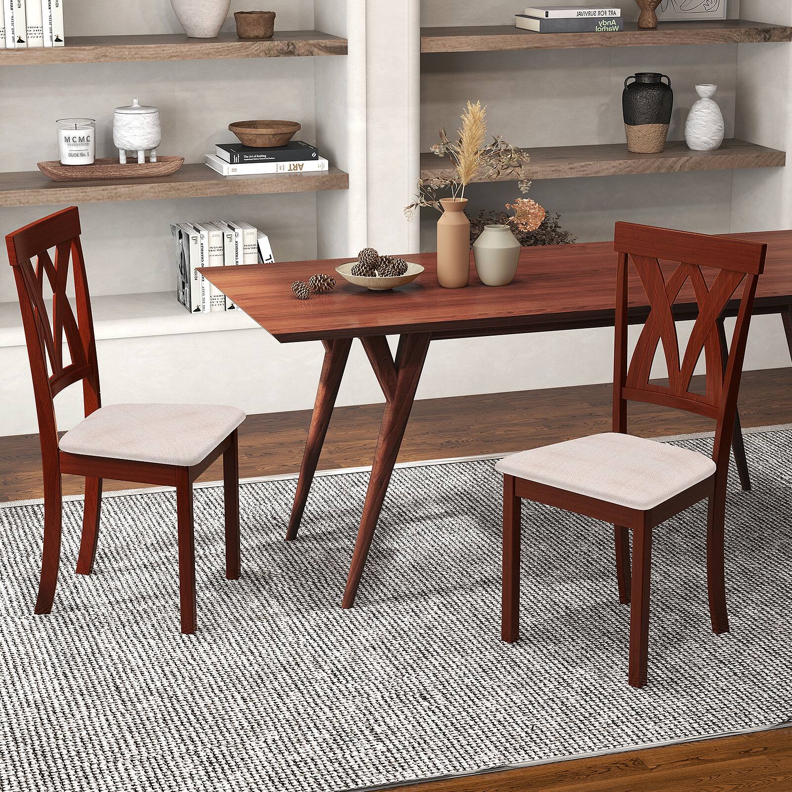 The image shows a wooden dining table with four wooden chairs surrounding it. The table is set with a vase, a bowl, and a book. The chairs are arranged in a way that they are facing each other, creating a comfortable and inviting atmosphere for a meal or a conversation. The table is placed on a rug, adding to the cozy and warm ambiance of the space.