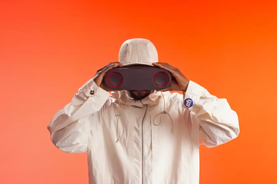 FYI, the man in the image is wearing a white jacket and a white hat, and he is holding a black object in front of his face.