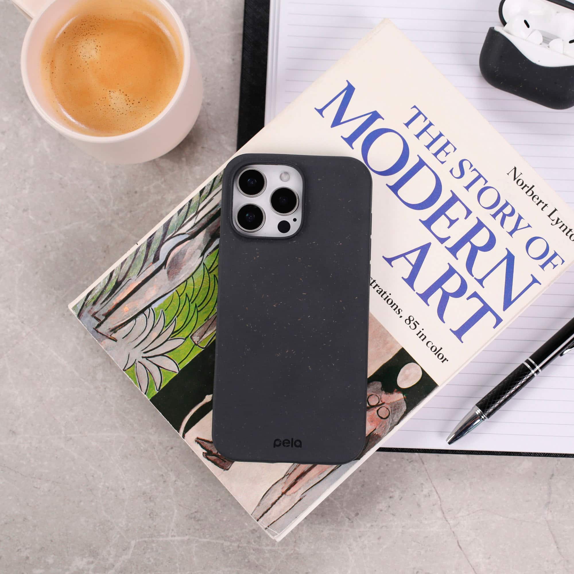 The Modern Story of Art by Norbert Lynch is a book about art and its various interpretations. The book is placed on a table next to a cup of coffee and a cell phone. The cell phone is covered in a black case, and the book is accompanied by a notebook and a pen.