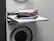 A white washing machine with a shelf on top of it holding a pile of clothes.
