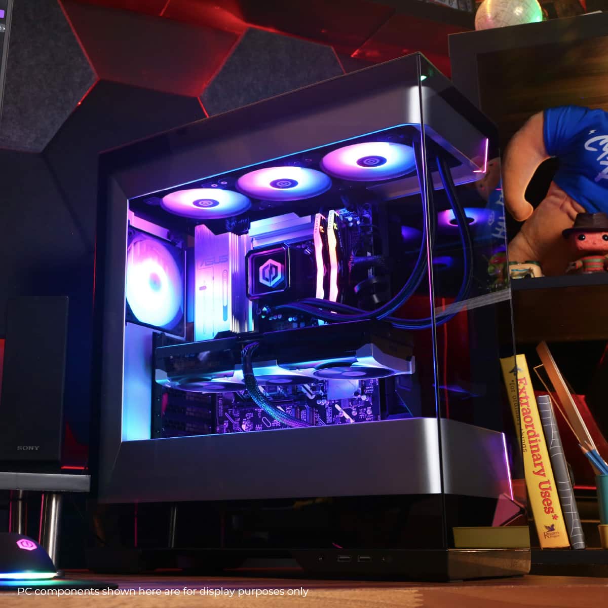 The image features a computer tower with a blue light inside. The tower is surrounded by various books and a person is visible in the background. The image is likely showcasing the computer tower and its components for display purposes.