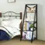 The image features a bed with a black metal headboard and a black bookshelf next to it. The bookshelf is filled with various books, including a collection of travel books. There is also a small potted plant on the bookshelf, adding a touch of greenery to the space. The bed is covered with a blue comforter, and there are two pillows on it. The arrangement of the bed and bookshelf creates a cozy and inviting atmosphere in the room.