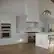 The image shows a large, clean, and modern kitchen with white cabinets and a white island. The kitchen is equipped with a stove, oven, and refrigerator. There is also a sink and a dining table with a chair. The kitchen is well-lit, and the cabinets are white, giving the space a bright and airy feel.