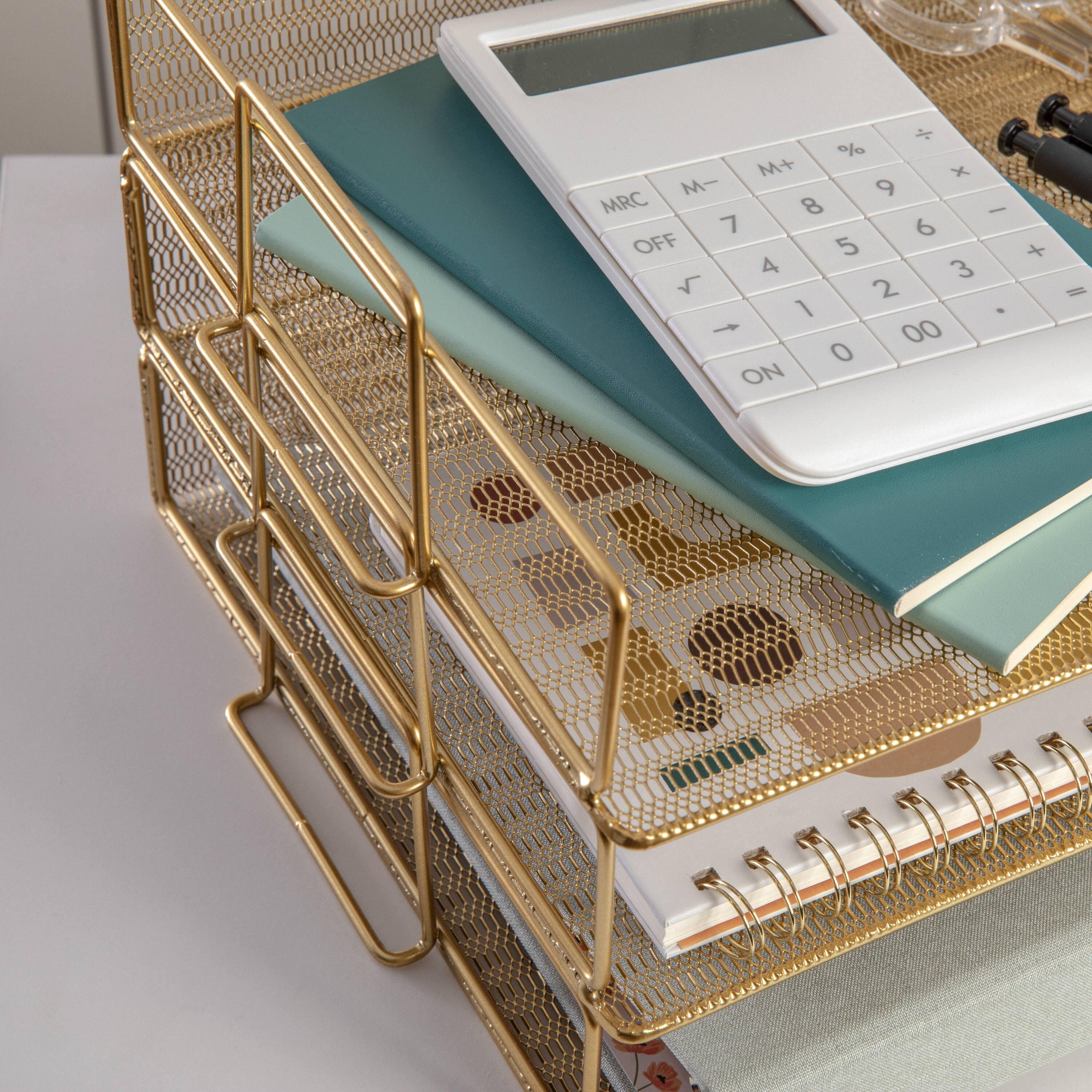 The image shows a white calculator placed on top of a stack of books, with a blue notebook nearby. The calculator has a gold frame and is positioned next to a spiral notebook. The books are arranged in a stack, with the calculator resting on top of them.