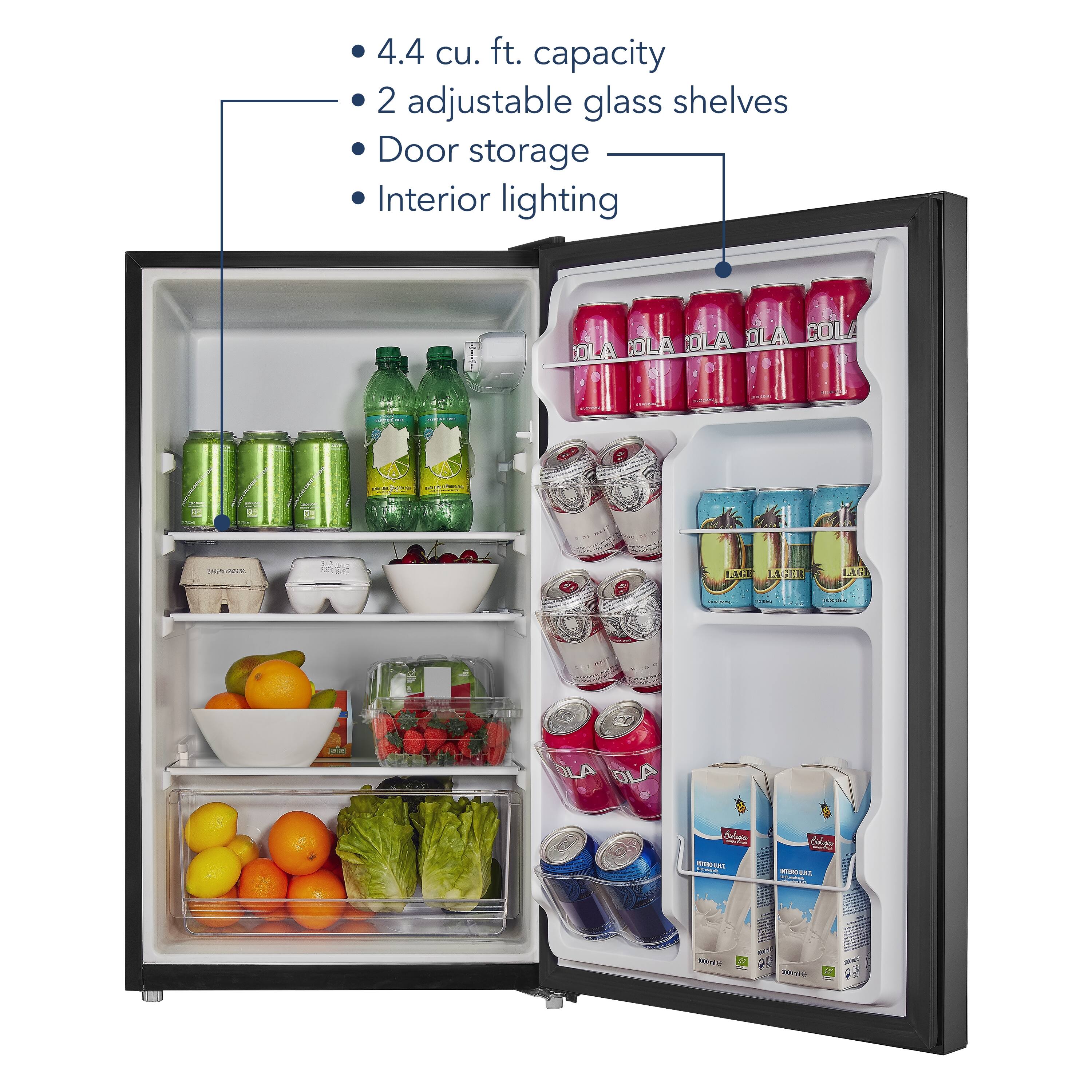 The image shows a refrigerator with a capacity of 4.4 cu. ft. It has two adjustable glass shelves and door storage. The interior of the refrigerator is illuminated by a light. The refrigerator is filled with various items, including several bottles of Ola Cola, a bowl of fruit, and a few other items.
